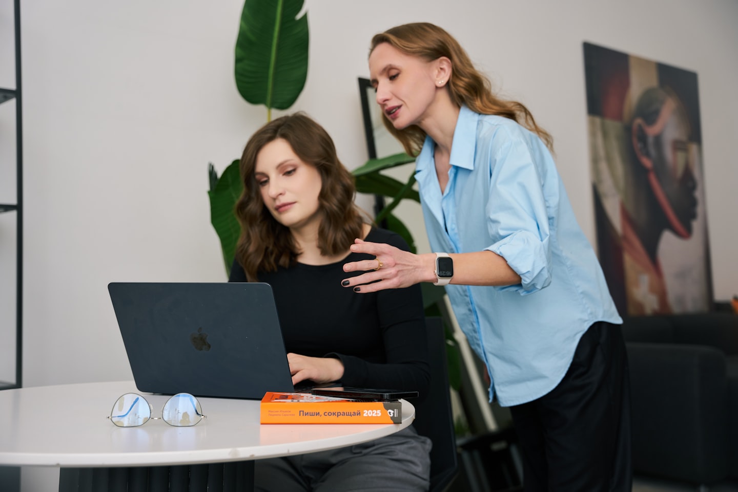 Two businesswomen collaborate while looking at a laptop screen.
